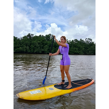 Woman paddleboarding on calm water wearing a purple wetsuit.