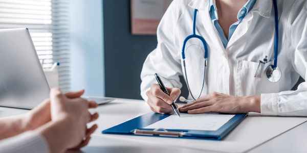 A doctor peaking to a patient.  Close up of doctor writing on a document on a clipboard.