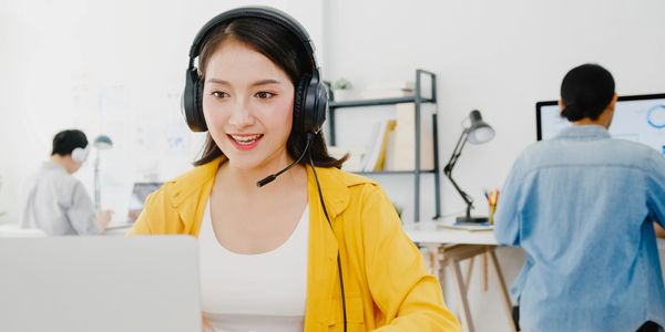 Young woman wearing headset working on laptop in a bright office.