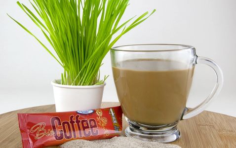 A cup of Bio Coffee alongside  wheatgrass and a single satchet.