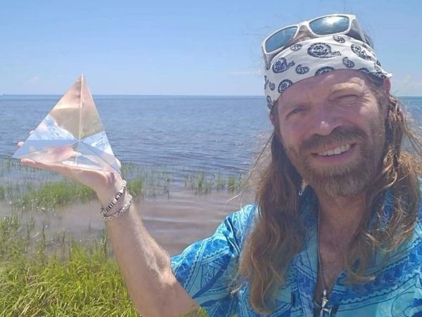 Man holding a glass pyramid by a lakeside, smiling.