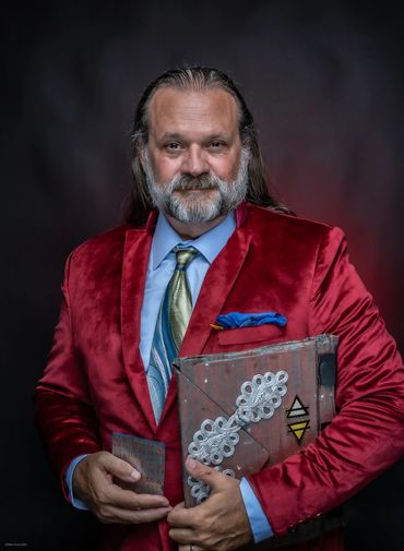 Man in a red velvet blazer holding a decorated book with a confident smile.