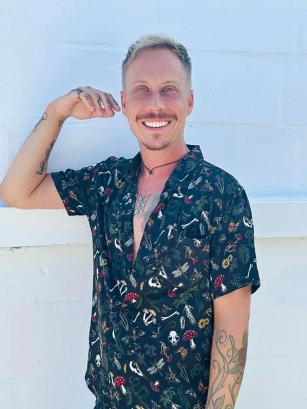 Smiling man in a patterned black shirt posing against a white wall.