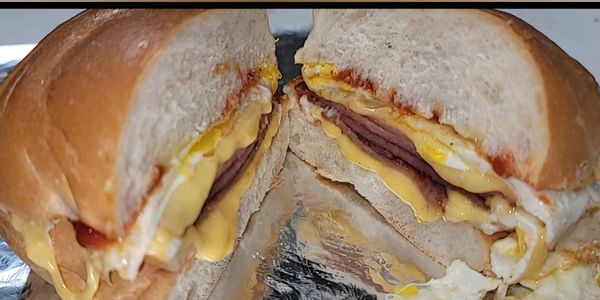 Close-up of a breakfast sandwich with egg, cheese, and meat on a bun.