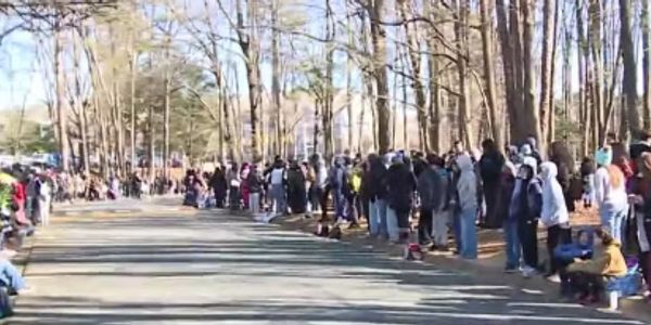 Crowd of people lined up along a road in a wooded area.