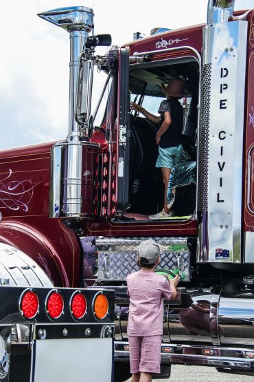 Two children exploring a large maroon semi-truck with shiny chrome details.