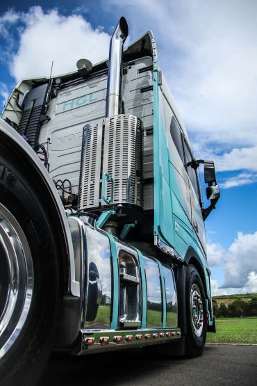 Close-up of a shiny, teal and chrome semi-truck against a blue sky.