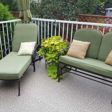Outdoor patio seating with green cushions and plants on a textured floor.