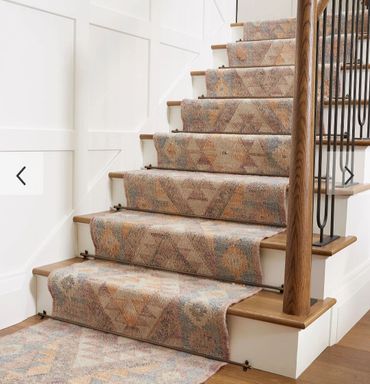 Staircase with patterned carpet runner secured by metal rods and wooden handrail.