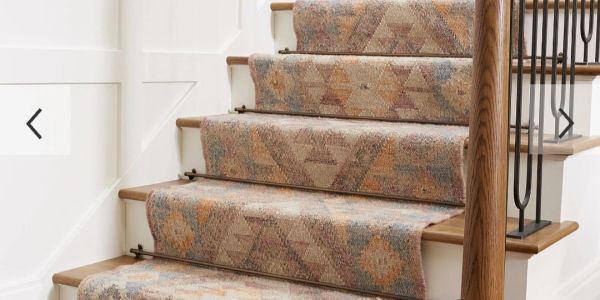 Staircase with patterned carpet runner secured by metal rods and wooden handrail.