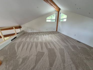 Empty attic room with new patterned carpet and white walls.