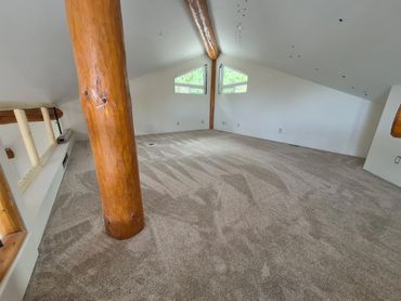Spacious attic room with beige carpet and wooden beams.