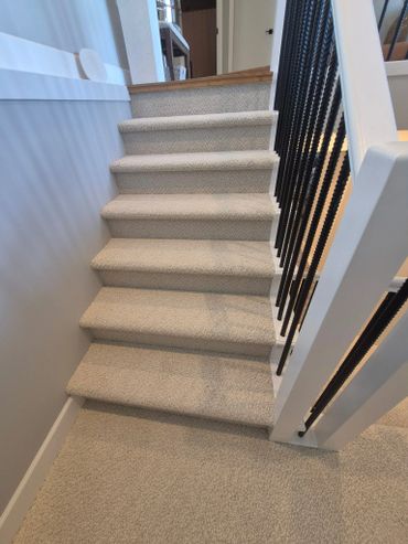 Carpeted staircase with black metal railings and white walls.