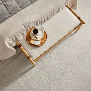Wooden bench with a coffee cup and a book beside a bed.