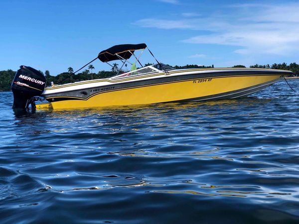 Yellow speedboat with Mercury engine floating on calm water under blue sky.