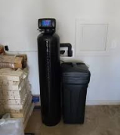 A black water softener system installed near a stack of firewood indoors.