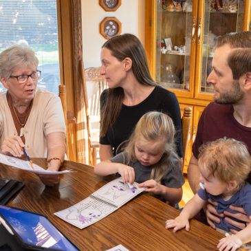 Family members engaged in a drawing activity around a table.