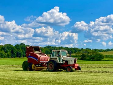 Case 1070 tractor pulling a New Holland RB 450 round baler baling hay on a sunny day.