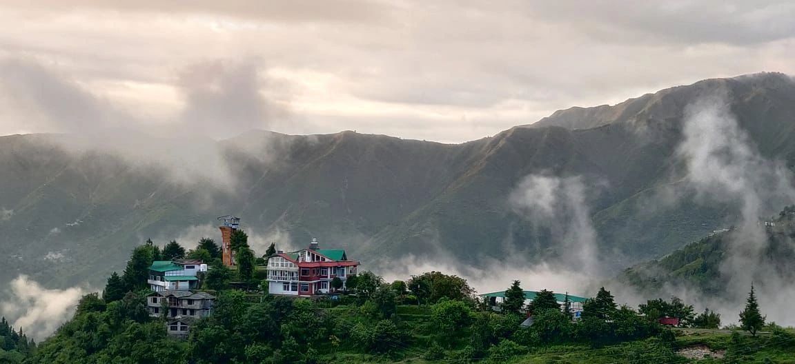 Misty mountains with houses perched on a lush green hill.