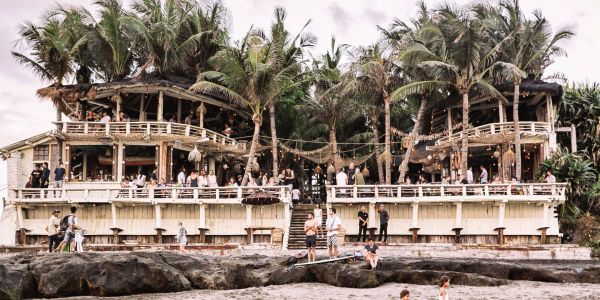 A tropical beach bar with people enjoying the atmosphere under palm trees.