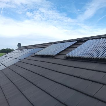 Dak met zonnepanelen en zonnecollectoren onder blauwe lucht.