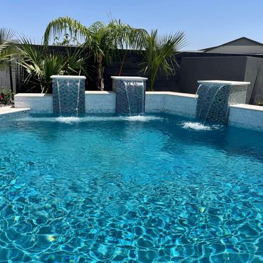 Modern pool with cascading water features and palm trees under a clear sky.