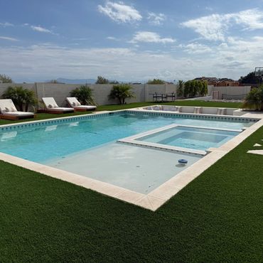 Modern backyard pool with lounge chairs and clear blue water under a partly cloudy sky.
