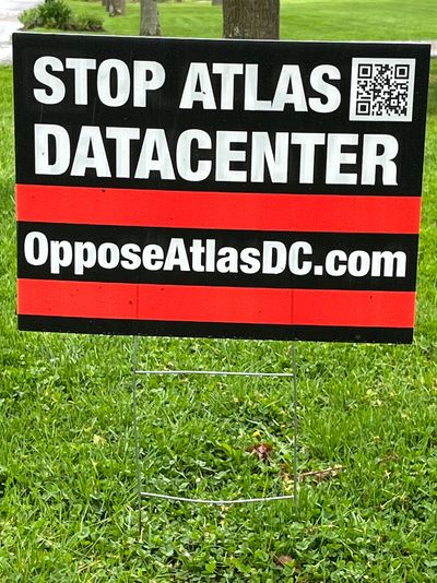 Protest sign against Atlas datacenter with website and QR code.