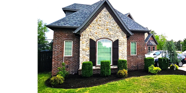 Brick house with stone facade and neatly trimmed shrubs in front.