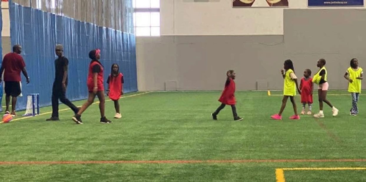 Children and adults playing indoor soccer in colored vests on artificial turf.