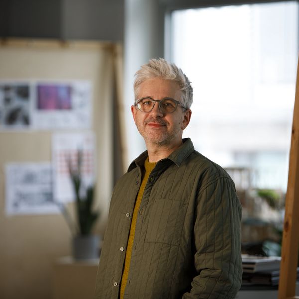 Smiling man with gray hair and glasses in a cozy indoor setting.