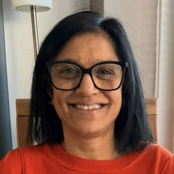 Smiling woman with glasses and black hair wearing an orange sweater.