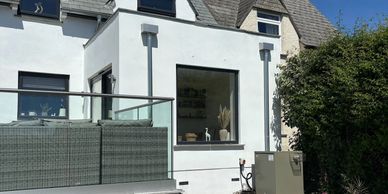 Modern house exterior with large window and gravel garden under bright sunlight.