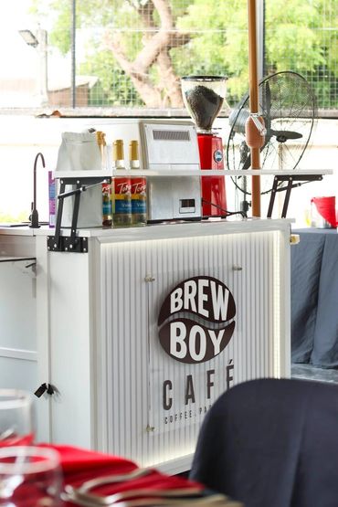 Coffee stand with Brew Boy Café branding and coffee equipment.