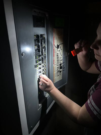 Person fixing circuit breaker with flashlight in dark.