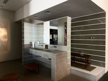 Bathroom remodel with light tan/gray stone countertop area with two sinks and a dark gray tile wall