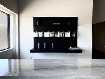Black shelving with lots of vases behind a gray stone or stone-like countertop in the foreground