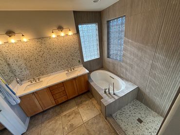 Bathroom remodel with brown cabinets, and a new tile shower, as well as a white tub
