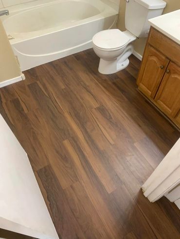 Bathroom remodel with rich brown plank flooring, with brown cabinets and tan walls and a white tub