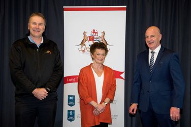 Three professionals pose in front of a banner with a coat of arms.