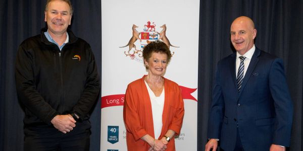 Three professionals pose in front of a banner with a coat of arms.