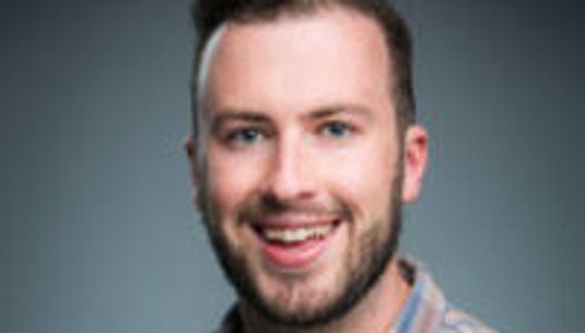 Smiling man with a beard and blue eyes in a casual shirt.
