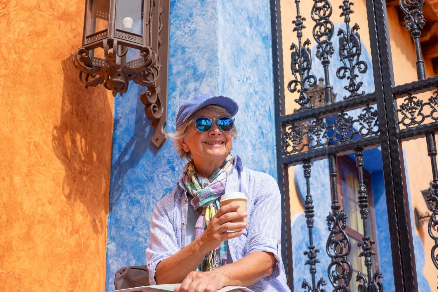Happy traveler holding a coffee in front of a decorative iron grate and bright blue and coral walls.