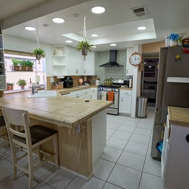 Bright kitchen with white cabinets, tiled countertops, and hanging plants.