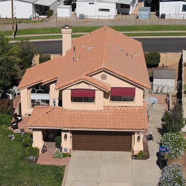 A two-story house with a terracotta tile roof and red window awnings.
