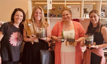 Four women smiling and holding glass terrariums with succulents indoors.