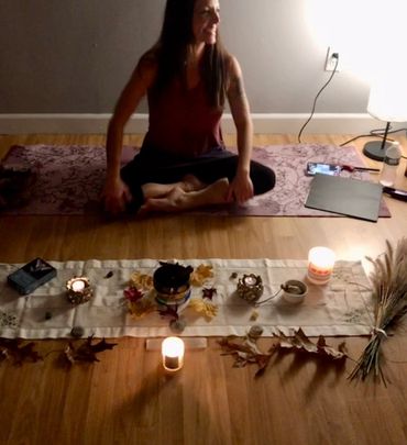 Woman sitting cross-legged on a yoga mat with candles and autumn decorations in front.