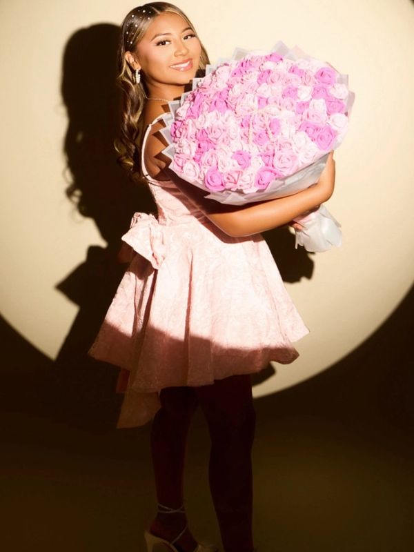 Young woman in pink dress holding a large bouquet of pink roses.