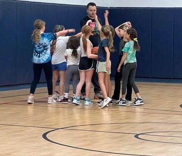 Coach giving instructions to a group of young girls in basketball practice.