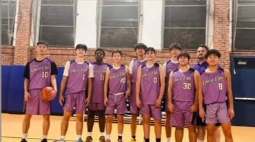 Youth basketball team posing in purple uniforms indoors.